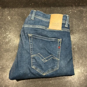 Replay Hyperflex jeans blå W30 L30 - Snygga blå Replay Hyperflex jeans med klassisk femficksdesign och kontrastsömmar. Jeansen har en skön stretchig känsla och normal passform. Märkespatch i läder baktill och diskret Replay-logga på fickan. Perfekta för dig som gillar stilrena och bekväma jeans.