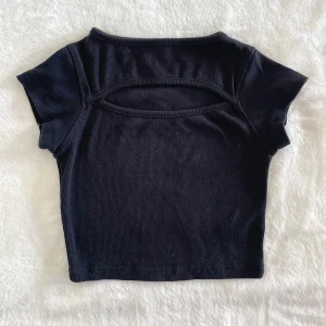 Svart croppad topp med cut-out Boohoo - Snygg svart croppad topp från Boohoo med korta ärmar och cool cut-out detalj på ryggen. Ribbad struktur i tyget ger en extra touch. Perfekt för dig som gillar trendiga och stilrena plagg med lite edge.