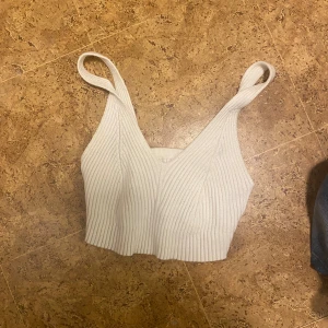 Vit ribbad croppad linnetopp - Säljer en vit croppad linnetopp med breda axelband och snygg v-ringning. Toppen är ribbad och stickad vilket ger en skön och trendig känsla. Perfekt att matcha med jeans eller kjol för en cool look.