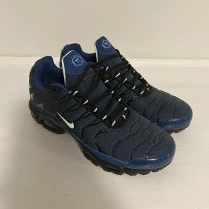 Nike sneakers blå mesh och svart - Snygga Nike sneakers i marinblå mesh med svarta och vita detaljer. Skorna har en sportig design med svarta vågformade linjer och en vit swoosh på sidan. Svart och blå sula med platt profil, samt svarta snören med vita inslag. Perfekta för dig som gillar streetwear.