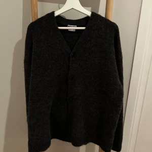 Mörkgrå kofta från Weekday *M* - Mysig mörkgrå kofta från Weekday i storlek M. Koftan har en enkel design med knappar framtill, v-ringning och lång ärm. Tillverkad i ett stickat material som känns både mjukt och varmt, perfekt för kyliga dagar.