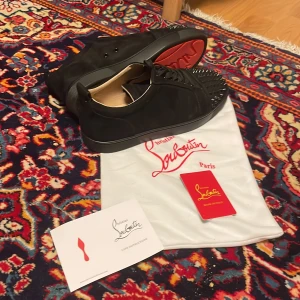 Christian Louboutin svarta sneakers med nitar - Svarta sneakers från Christian Louboutin i mocka med svarta nitar på tån och klassisk röd sula. Skorna har snörning och rund tå, samt exklusiv känsla med läderdetaljer invändigt. Perfekta för dig som vill sticka ut med en edgy och lyxig stil.