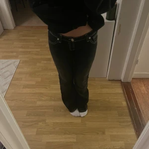 Svarta bootcut jeans från Gina Tricot - Svarta jeans från Gina Tricot med bootcut passform och låg midja. Snygga kontrastsömmar i vitt och dekorativa bakfickor med broderad detalj. Klassisk femficksmodell i stretchig bomullsblandning, perfekta för en trendig look.