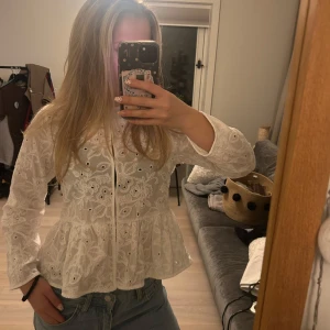 Vit spetsblus från Zara XS - Supersöt vit blus från Zara i storlek XS med broderade blommor och spetsdetaljer. Blusen har lång ärm, knappar framtill och en lätt volang nertill. Perfekt för dig som gillar romantisk och feminin stil. Endast används en gång!!