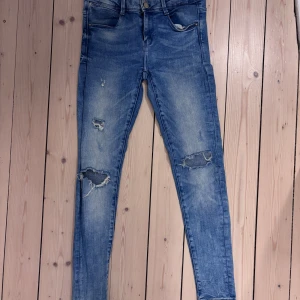 Blå skinny jeans från Zara Trafaluc - Snygga blå skinny jeans från Zara Trafaluc med slitna detaljer på knäna och låren. Jeansen har fem fickor, klassisk knapp och dragkedja framtill samt en ljus tvättad look. Perfekt för dig som gillar en trendig och avslappnad stil.