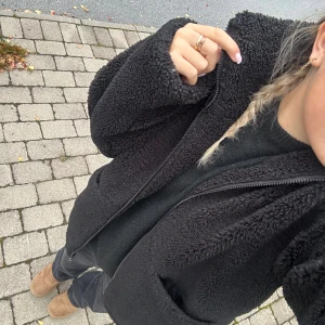 Svart teddyjacka från NA-KD - Mysig svart teddyjacka från NA-KD med dragkedja framtill och stora fickor. Jackan har en oversized passform och är perfekt för kyliga dagar. Tillverkad i mjukt teddy-material som ger en cool och avslappnad vibe.