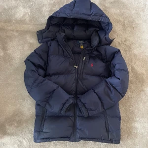 Mörkblå dunjacka från Polo Ralph Lauren - Säljer marin blå Ralph lauren jacka i fint skick 8/10 äkta såklart. Barn storlek XL passar dig som är 165-175 fits XS modellen är 178 lång, hör av er om minsta fundering!