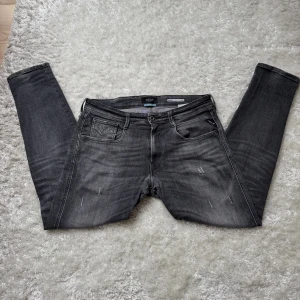 Replay anbass jeans - Säljer ett par gråa Replay anbass jeans i slim fit med snyggt slitna detaljer och klassiska fem fickor. Jeansen är i allmänt bra skick bara ett litet hål som syns på sista bilen. De är köpta från pondus för 1800kr och kvitto ska finnas. 