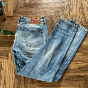 Replay rockxanne ljusblå slitna jeans - Säljer ett par ljusblå jeans från Replay med snyggt slitna detaljer och broderad patch med rosor på bakfickan. Jeansen har raka ben, klassisk femficksmodell och är tillverkade i mjukt denimtyg. Perfekta för en avslappnad och trendig look.