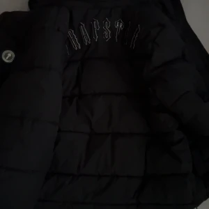 Svart pufferjacka från Trapstar - Säljer en svart pufferjacka från Trapstar med broderad logga i vitt på ryggen och Jackan har en schysst oversized look och är perfekt för kalla dagar. Materialet är syntet och jackan har långa ärmar. Fråga om du vill ha fler bilder köpte den för 1700 har haft i ungefär 2veckor men säljer för den va lite liten för mig perfekt för folk som har storlek m-s pris kan diskuteras 