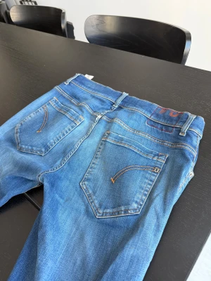 Dondup jeans i storlek 34 - Säljer ett par dondup med slitningar och hål på benen. Jeansen har klassisk femficksdesign, orangea sömmar och en snygg tvättad look. Passar dig som gillar en avslappnad och trendig stil. Materialet är jeans och modellen är rak med normal passform.
