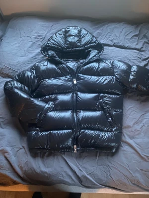 Svart pufferjacka från ZARA - Säljer en svart, glansig pufferjacka från ZARA med huva och dragkedja. Jackan har en oversized look, breda kanaler och två sidofickor med dragkedja. Perfekt för kalla dagar och riktigt snygg till streetwear. Den är vattentät och håller dig extremt varm hela vintern, nypris är ca 1000kr! Om du har frågor är de bara att skriva😀😀( den har en diskret vattentät patch på höger insida ärm då min hund ber sönder och jag fick gå till en skräddare och få den sydd)