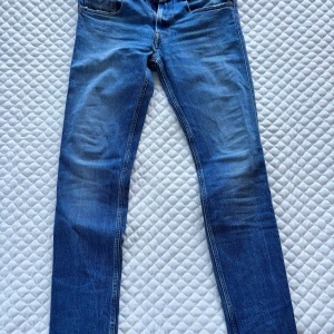 Replay Anbass blå jeans herr 31/32 - Snygga blå Replay Anbass jeans med klassisk femficksdesign och slitna detaljer. Jeansen har raka ben, normal passform och är tillverkade i slitstarkt denim. Märkespatch bak i midjan och diskret Replay-logga vid fickan. Perfekta för en laidback look!