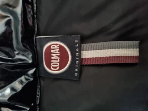 Svart pufferjacka från Colmar - Snygg svart pufferjacka från Colmar Originals med glansig finish och hög krage. Jackan har dragkedja framtill, två sidofickor med dragkedja och Colmar-logga på ärmen. Perfekt för dig som gillar streetstyle och vill hålla dig varm med stil.