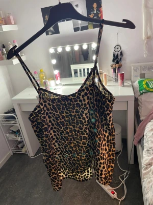 Leopardmönstrad kort klänning med smala axelband - Säljer en snygg kort klänning med leopardmönster och smala axelband. Klänningen har en loose passform och är tillverkad i ett lätt, glansigt material som ger en cool vibe. Perfekt för dig som gillar att sticka ut med djurmönster och vill ha något bekvämt och trendigt.