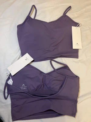 2st Lila sport BH från La Nikar - Supersnygg lila linnetopp från La Nikar med smala axelband och croppad passform. Toppen är tillverkad i mjukt syntetmaterial som känns skönt mot huden. Perfekt för träning eller chill dagar. Enkel design utan mönster, med diskret logga framtill.