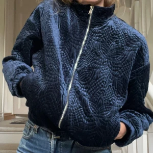 Mörkblå quiltad sammetsjacka  - Mönsterquiltad kofta/jacka i mörkblå skiftande sammet med silvrig dragkedja och fickor. Ovanligt kollektionsplagg från Lindex. Snörning i nederkant så att modellen kan stylas med lösare nedre mudd om man vill. Ej fodrad. Kan bäras som inneplagg el jacka - praktiskt köp! Knappt använd. 