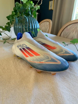 Adidas F50 fotbollsskor blå/röd - Säljer ett par Adidas F50 fotbollsskor med snygg design i blått, vitt och rött. Skorna har en strömlinjeformad siluett, platt sula med dobbar och är tillverkade i syntetmaterial med Sprintweb-teknologi Använda i max 4 månader 