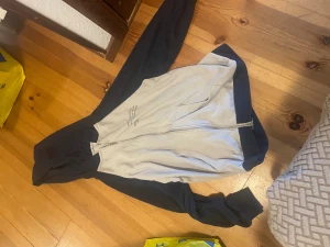 Beige och marinblå bomberjacka med tryck - Säljer en beige och marinblå bomberjacka med coolt texttryck på framsidan. Jackan har långärmade svarta ärmar, beige kropp och dragkedja framtill. Materialet känns som bomull och polyester, perfekt för dig som gillar streetstyle och vill sticka ut.