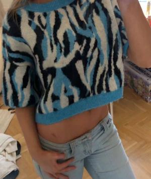 Blå croppad stickad zebra mönster!  - Säljer en croppad stickad tröja med blått, svart och vitt zebramönster. Tröjan har korta ärmar och ribbad kant vid hals och nederdel. Den är i stl M men jag skulle säga att den passar S med! 