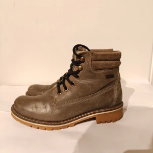 Tamaris boots - Robusta bruna boots från Tamaris med snörning och grov sula. Ovandel i skinn och detaljer i mocka vid skaftet. Fodrade med mjukt material för extra värme. Perfekta för kyliga dagar och har en klassisk, tidlös look.