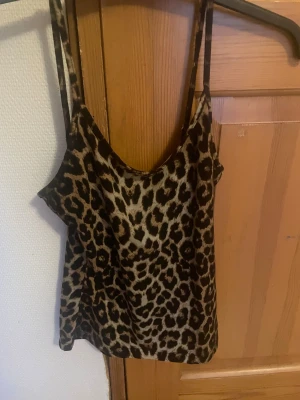 Leopardmönstrad linnetopp från SHEIN - Säljer en snygg leopardmönstrad linnetopp från SHEIN i storlek XS. Toppen har tunna axelband och ärmlös design, perfekt för dig som gillar djurmönster och vill sticka ut. Färgerna går i beige och brunt med svarta leopardfläckar. Materialet känns lätt och smidigt.