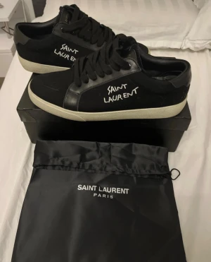 Saint Laurent skor - Svarta sneakers från Saint Laurent med vit broderad logga på sidan. Använt bara några gånger, väldigt fina skor STORLEK 42 OCH PASSAR 43 perfekt ”är 43”