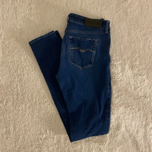 Blå Replay jeans med raka ben - Säljer ett par snygga blå jeans från Replay med klassisk femficksdesign och raka ben. Jeansen har diskreta slitningar framtill, guldfärgade sömmar och logga på bakfickan. Perfekt passform och sköna att bära, tillverkade i mjukt denimtyg strlk w29 L32