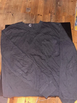 Svart långärmad tröja från C - Svart långärmad tröja från C Organic Cotton i ekologisk bomull. Tröjan har en enkel design med rund hals och en bröstficka på vänster sida. Perfekt för chill dagar och enkel att matcha med jeans eller joggers.