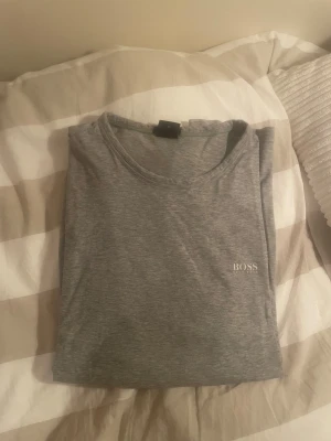 Grå tröja från Hugo Boss - Snygg grå tröja från Hugo Boss med diskret logga på bröstet. Tröjan har rund hals och är tillverkad i mjuk bomull som känns skön mot huden. Perfekt för dig som gillar stilrena och enkla plagg med en touch av lyx.