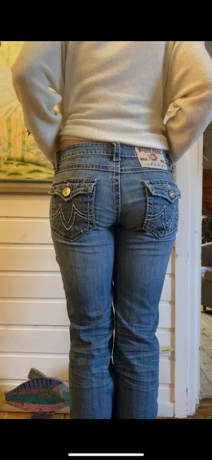 Bisou Deve blå jeans med fickdetaljer - Snygga blå jeans från Bisou Deve med låg midja och raka ben. Jeansen har markerade vita sömmar, coola ficklock med knappar bak och tydliga fickdetaljer fram. Materialet är klassisk denim och passformen är normal. Perfekt för dig som gillar statement-jeans.