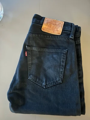 Svarta Levi's 501 jeans - Svarta Levi's 501 jeans med klassisk femficksdesign och ikonisk läderpatch bak i midjan. Jeansen har rak passform och är tillverkade i slitstarkt bomullsmaterial. Perfekta för dig som gillar tidlös stil och vill ha ett par jeans som funkar till allt.