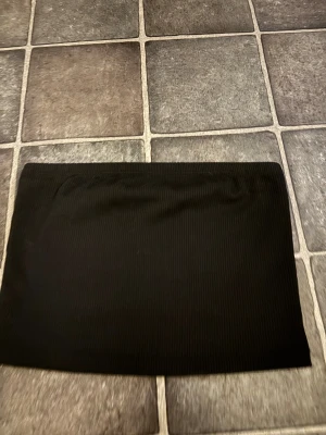 Svart ribbad tub topp XS - Svart ribbad tub topp i storlek XS. Tub toppen  har en enkel, tight passform och är gjord i ett stretchigt material som sitter snyggt på kroppen. Perfekt för dig som gillar minimalistisk stil och vill ha en basic tub topp  som funkar till många olika looks.