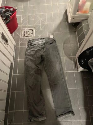 Grå Replay jeans straight fit - Säljer ett par gråa Replay jeans med klassisk femficksdesign och raka ben. Jeansen har tydliga sömmar på bakfickorna och en neutral tvätt som passar till det mesta. Materialet är slitstarkt denim och modellen sitter normalt över höfterna.