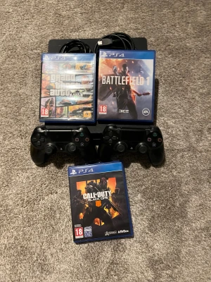 Playstaion 4 Slim 500GB med 2 kontroller och 3 spelspel - Sony PlayStation 4 Slim 500GB i bra skick, med två originalkontroller och tre populära spel: GTA V, Battlefield 1 och Call of Duty Black Ops 4. Konsolen har mindre yttre slitage men fungerar utmärkt. Perfekt för spelkvällar med vänner! Kablar ingår även!!