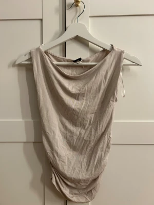 Beige ärmlös topp från Gina Tricot - Säljer en ljusbeige ärmlös topp från Gina Tricot i storlek XS. Toppen har en mjuk, draperad form med bred halsringning och är tillverkad i ett tunt, stretchigt bomullsmaterial. Perfekt för dig som gillar minimalistisk och clean stil.