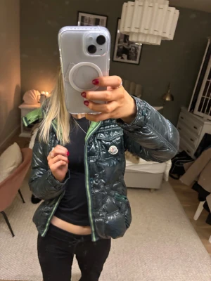 Grön Moncler pufferjacka med huva - Säljer en mörkgrön glansig pufferjacka från Moncler med limegrönt foder och huva. Jackan har dragkedja framtill, två fickor och klassisk Moncler-logga på bröstet. Perfekt för kalla dagar och riktigt snygg streetstil. Har tyvärr inte äkthetsbevis. Skriv för fler bilder o info❣️