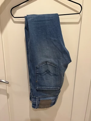 Replay Anbass blå jeans, storlek 31/32 - Snygga Replay Anbass jeans i klassisk blå tvätt med diskret slitning och raka sömmar. Modellen har fem fickor, smal passform och tydliga Replay-detaljer på bakfickorna. Stretchigt material för extra komfort och stil.