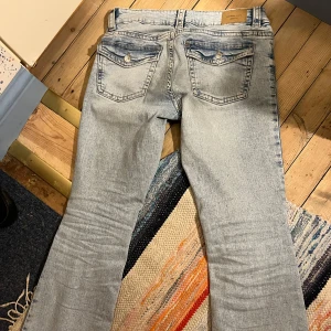Ljusblå bootcut jeans från Gina Tricot - Snygga ljusblå jeans från Gina Tricot med bootcut-ben. Jeansen har en låg midja och är tillverkade i mjukt denim-material. Fickorna bak har lock och knappdetaljer. Storlek 38. Inte mycket använda.