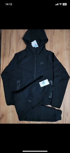 Svart Nike Tech Fleece hoodie - Nike Tech Fleece hoodie i svart med hel dragkedja, två sidofickor med dragkedja och stilren Nike-logga på bröstet. Hoodien har en modern passform och är tillverkad i mjukt fleece-material som är både lätt och värmande. Perfekt för en chill och sportig look.
