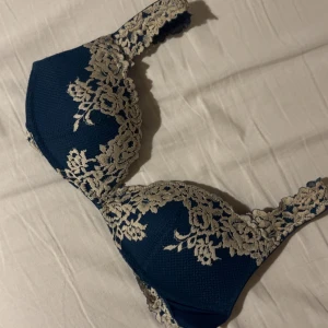  Blå intimissimi bh - Säljer en snygg blå korsett med beige spetsbroderi i blommigt mönster. Toppen har vadderade kupor och justerbara axelband för perfekt passform. Spetsen ger en lyxig känsla och gör den extra fin. Perfekt för dig som vill ha något unikt och elegant.