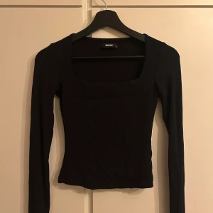 Svart ribbad topp från Bik Bok - Säljer en svart långärmad topp från Bik Bok med fyrkantig halsringning. Toppen är ribbad och har en slim passform som sitter snyggt på kroppen. Perfekt att styla med jeans eller kjol för en clean look.