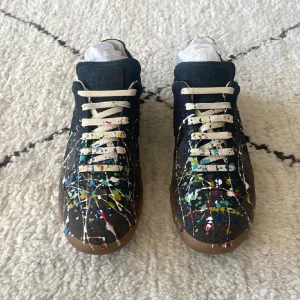 Maison Margiela GATs Paint Edition - Säljer mina Maison Margiela GATs i den ikoniska paint-splatter-designen. De är helt nya och aldrig använda, vilket syns tydligt på bilderna. Köpta från Farfetch och kvitto finns så klart.  Det här är en av Margielas mest eftertraktade modeller just nu – svåra att få tag på och ofta slutsålda. Klassisk GAT-silhuett i svart mocka och läder med handmålade färgstänk som gör varje par unikt.  Dustbags, originalbox och alla tags följer med. Perfekta för dig som gillar lyxiga sneakers med lite edge.