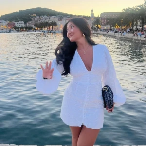 Adoore vit klänning - Säljer en vit kort klänning med v-ringning och puffiga långärmar. Klänningen har omlottstil, knappar framtill och markerad midja som ger en snygg siluett. Perfekt för sommarkvällar och har en lätt, luftig känsla. Passar dig som gillar stilrena och trendiga plagg. Obs sista knappen är sönder men går att fixa 