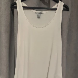 Vit ribbad linnetopp från H&M - Säljer en vit ribbad linnetopp från H&M i storlek M. Toppen har rund halsringning och ärmlös design, perfekt för att styla med jeans eller shorts. Materialet är mjukt och stretchigt för en skön passform. Enkel och clean look som funkar till många outfits.
