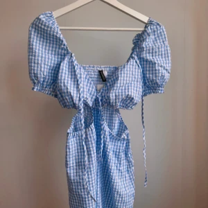 Söt sommarklänning - Jättesöt och somrig klänning i ljusblått och vitt rutmönster från HM Divided. Har knytning framtill och cut outs i midjan. Storlek 42, dock väldigt liten i storlek, passar mig som är en 38a. Helt ny med prislapp kvar, endast testad.