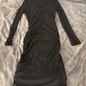 Svart ribbad långärmad klänning  - Svart ribbad klänning från Shein i storlek M. Klänningen har lång ärm, v-ringning och en snygg slits på sidan. Den är figurnära och har en stilren look som passar perfekt när du vill känna dig extra snygg.