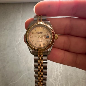 Datejust guld och silver klocka -  Datejust med tvåfärgad länk i guld och silver. Urtavlan är champagnefärgad med glittrande stenar som timmarkeringar och datumvisning. Boetten har räfflad guldkant och kronan är i guld. Länken är klassiskt Jubilee-stil.