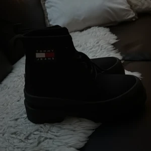 Svarta boots från Tommy Jeans - Säljer ett par svarta boots från Tommy Jeans med chunky sula och snörning framtill. Skorna har rund tå och är tillverkade i ett textilmaterial. Klassisk Tommy Jeans-logga på sidan i rött, vitt och blått. Perfekta för dig som gillar en stilren och urban look. Storlek 37 men det gick inte att ändra så det står 36 2/3