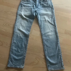 Levi's 514 ljusblå jeans straight fit - Ljusblå Levi's 514 jeans med klassisk straight fit. Jeansen har fem fickor, normal midja och snyggt slitna detaljer. Tillverkade i bomull med Levi's ikoniska läderpatch och röd etikett bak. Perfekta för en avslappnad och stilren look.